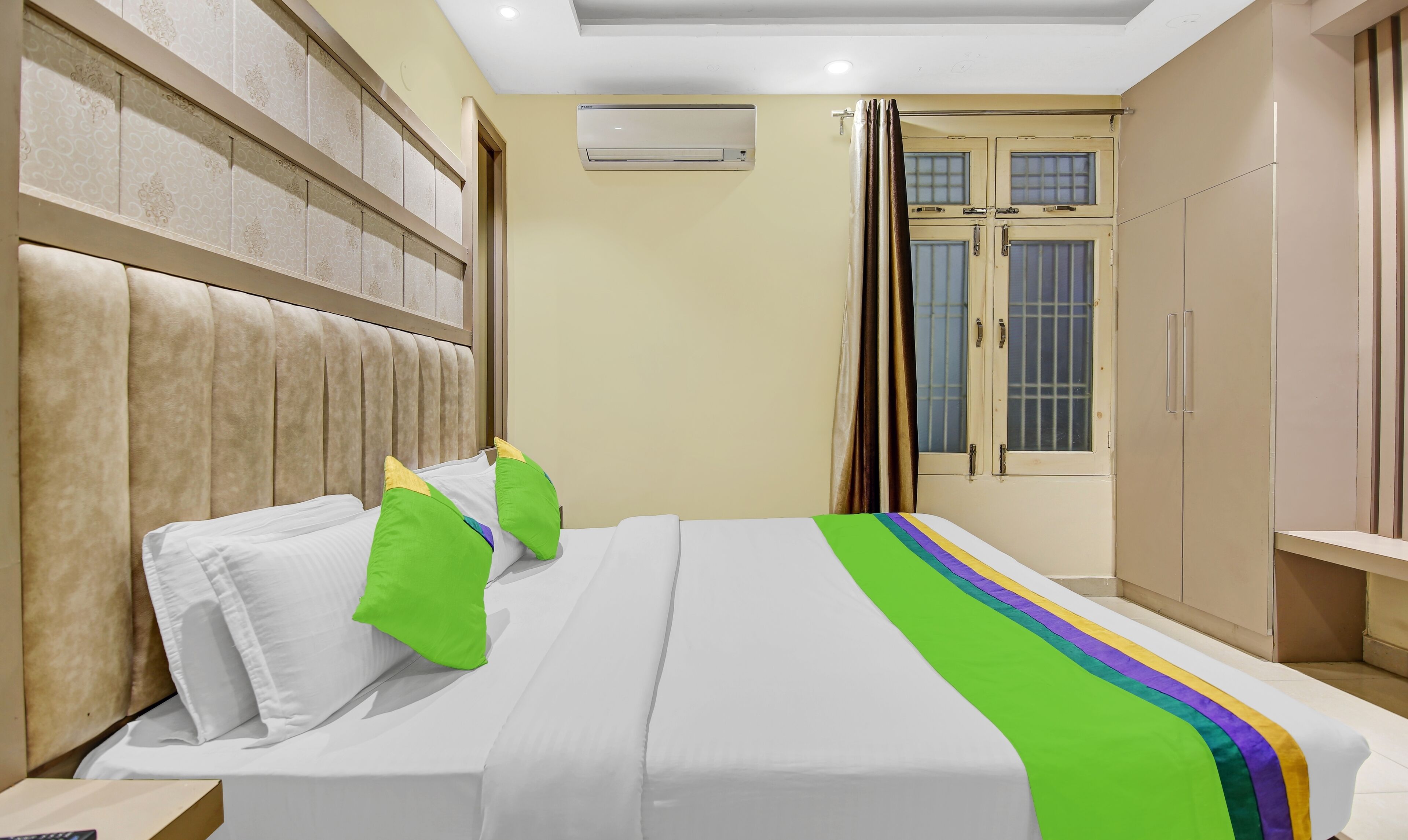 A hotel room with a bed, a headboard, a wardrobe, and a window with curtains.