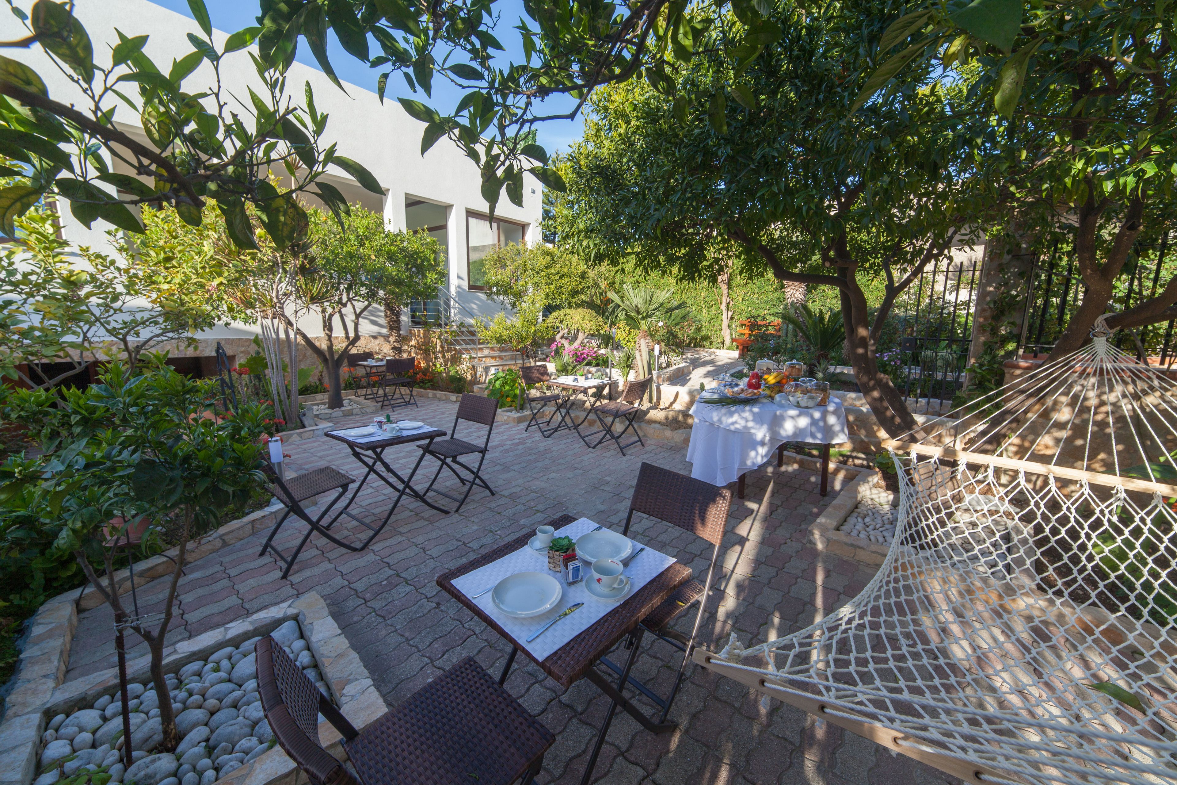 An outdoor patio with tables and chairs, surrounded by trees and plants.