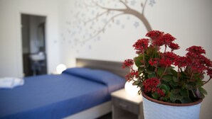 Une chambre à coucher avec un lit, une table de chevet et une plante en pot ornée de fleurs rouges.