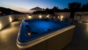 Un bain à remous avec un revêtement extérieur en bois, entouré de meubles d’extérieur et surmonté d’un grand parasol.