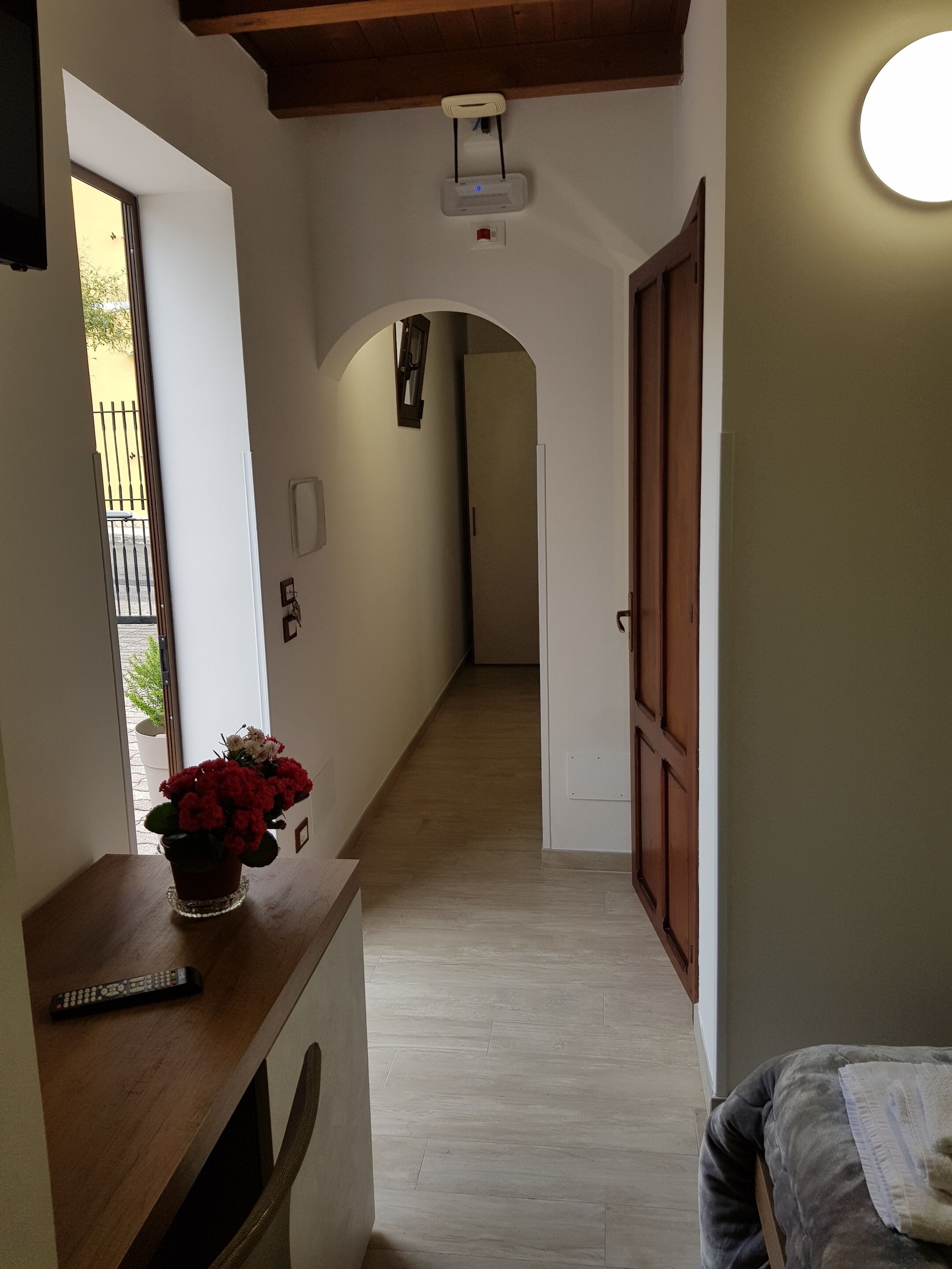 A hallway with a wooden bench, a potted plant, a remote control, and a door leading to another room.