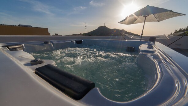Un bain à remous sur un toit-terrasse, avec vue sur une montagne et le soleil se couchant à l’horizon.
