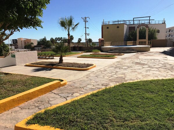 A paved courtyard with landscaped areas, palm trees, and a building with a balcony.