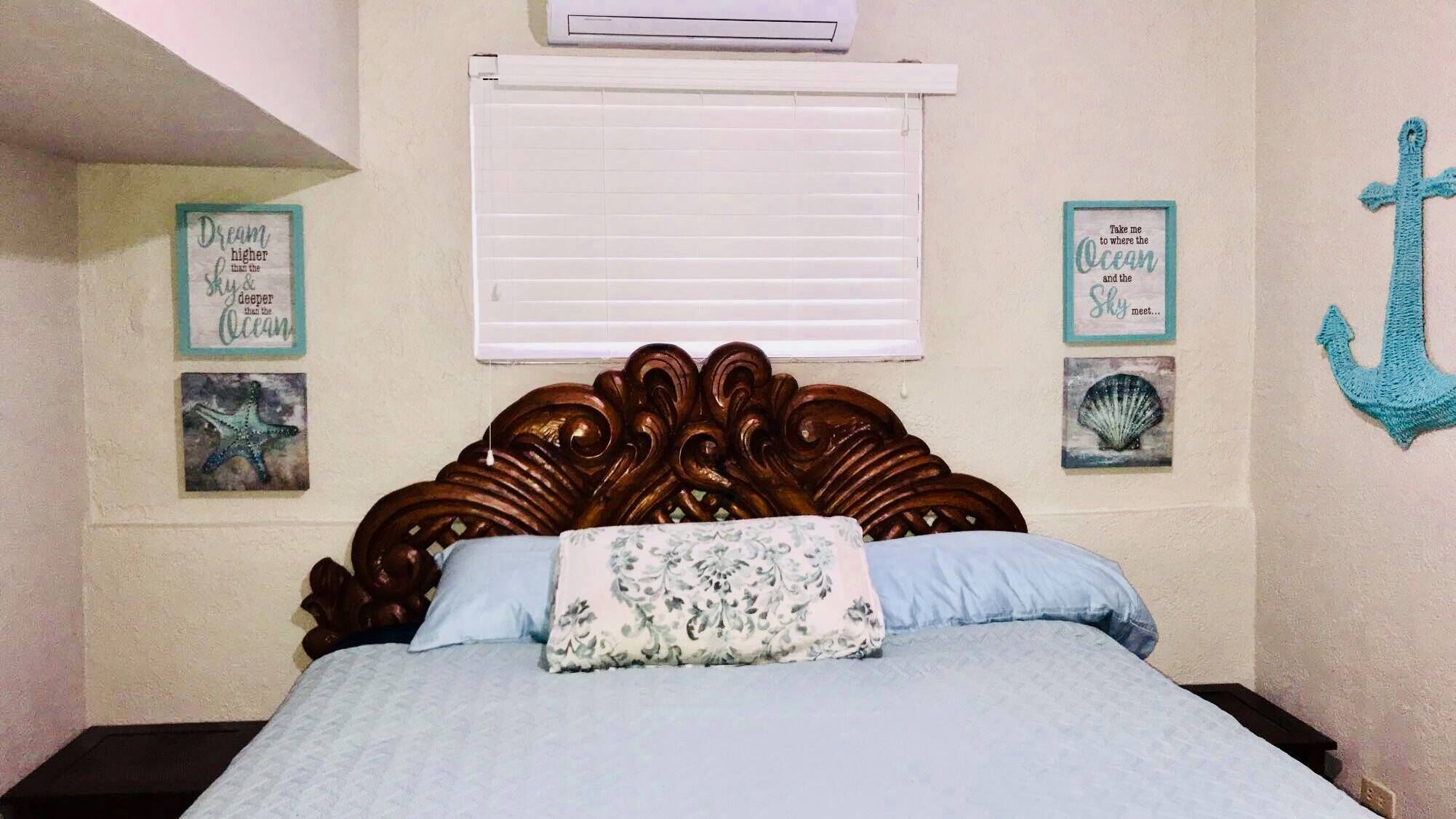 A bedroom with a wooden headboard, a bed with blue bedding, and wall decorations including framed text and an anchor.