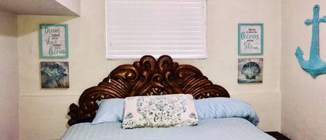 A bedroom with a wooden headboard, a bed with blue bedding, and wall decorations including framed text and an anchor.