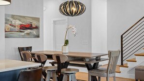 Un comedor con una mesa y sillas de madera, una lámpara colgante y un cuadro en la pared.
