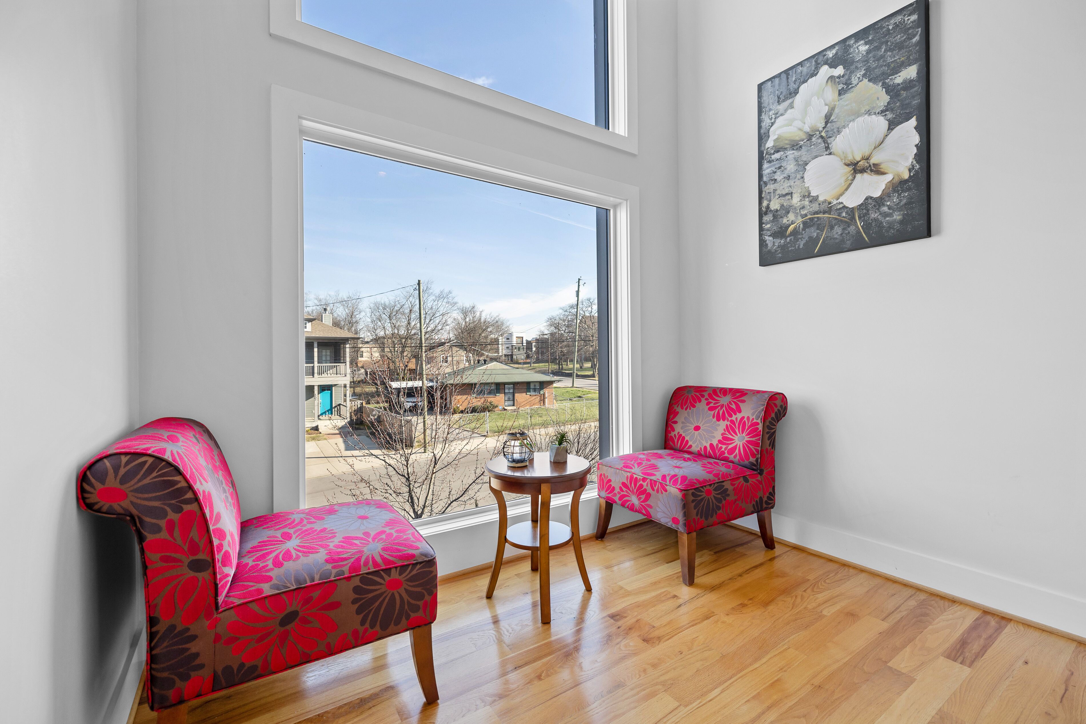 Una habitación con dos sillones de estampado floral, una mesita de madera y un ventanal que ofrece vistas a edificios y árboles.
