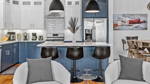 Una cocina moderna con armarios blancos y azules, una isla central con taburetes y un comedor con mobiliario de madera.