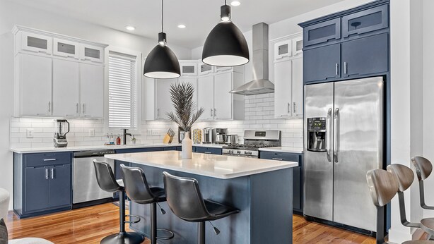 Una cocina moderna con una isla central, taburetes de bar, electrodomésticos de acero inoxidable y un refrigerador grande.
