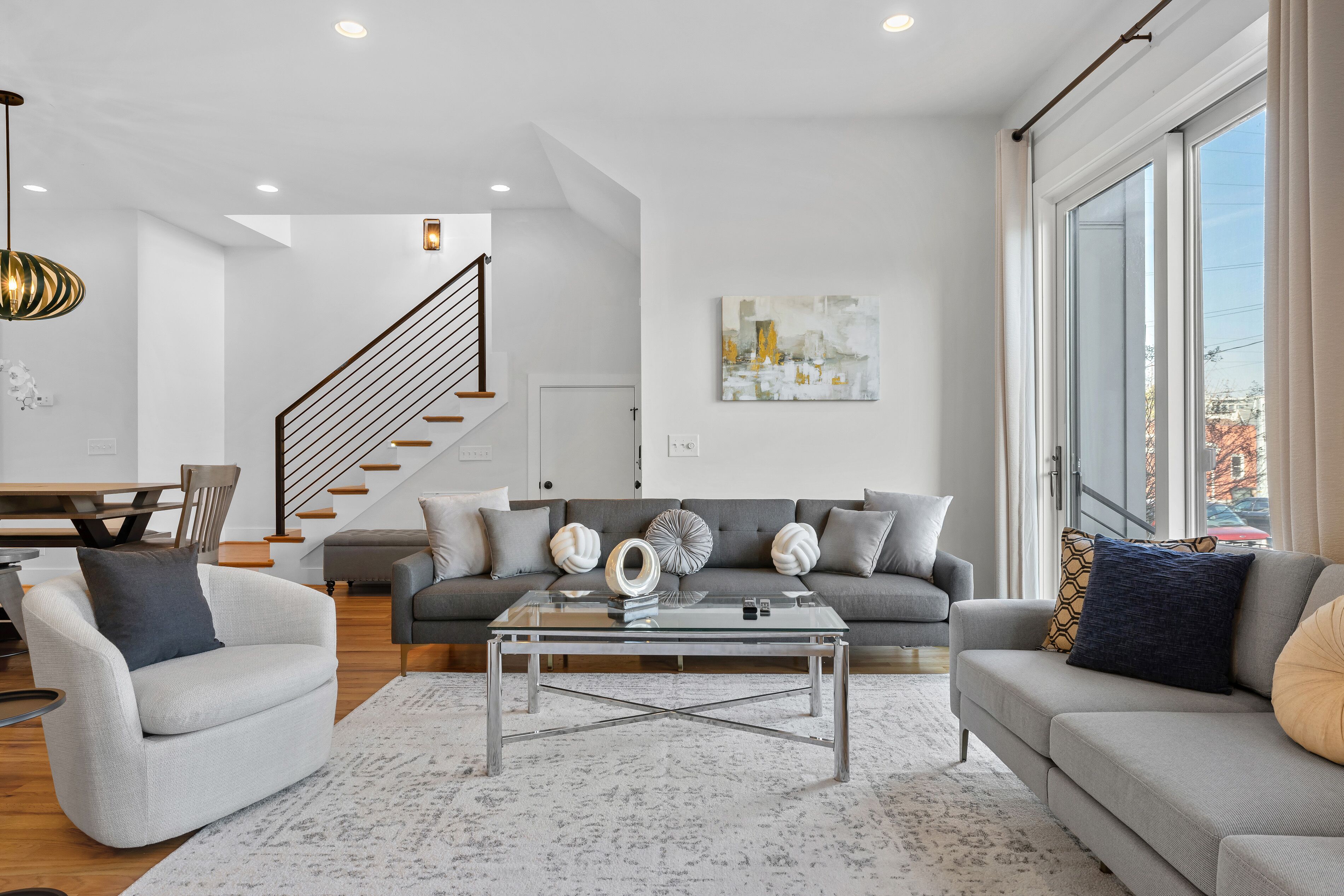 Ein modernes Wohnzimmer mit einer Couch, Sesseln, einem Couchtisch und einer Treppe.