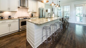 A modern kitchen with white cabinets, stainless steel appliances, and a large island with bar stools. - ☀️WaterSound 30A- Walk 2 Beach-Bikes-Pool-Anchors Up (Santa Rosa Beach)