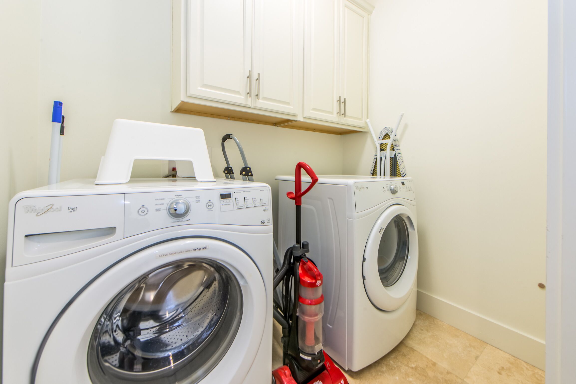 A laundry area with two washing machines and a red vacuum cleaner.