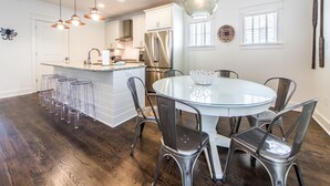 A modern kitchen with a central island, stainless steel appliances, and a dining area with a glass table and metal chairs. - ☀️WaterSound 30A- Walk 2 Beach-Bikes-Pool-Anchors Up (Santa Rosa Beach)