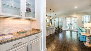 A kitchen with white cabinets, granite countertops, and a dining area with bar stools. - ☀️WaterSound 30A- Walk 2 Beach-Bikes-Pool-Anchors Up (Santa Rosa Beach)