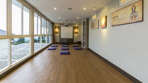 A spacious hallway with large windows, wooden flooring, and exercise mats arranged in rows. - Dhanesvara Holistic Villa (Batu)