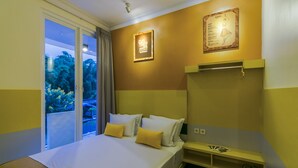 A hotel room with a bed, a nightstand, a shelf with glasses, and a poster on the wall. - Dhanesvara Holistic Villa (Batu)