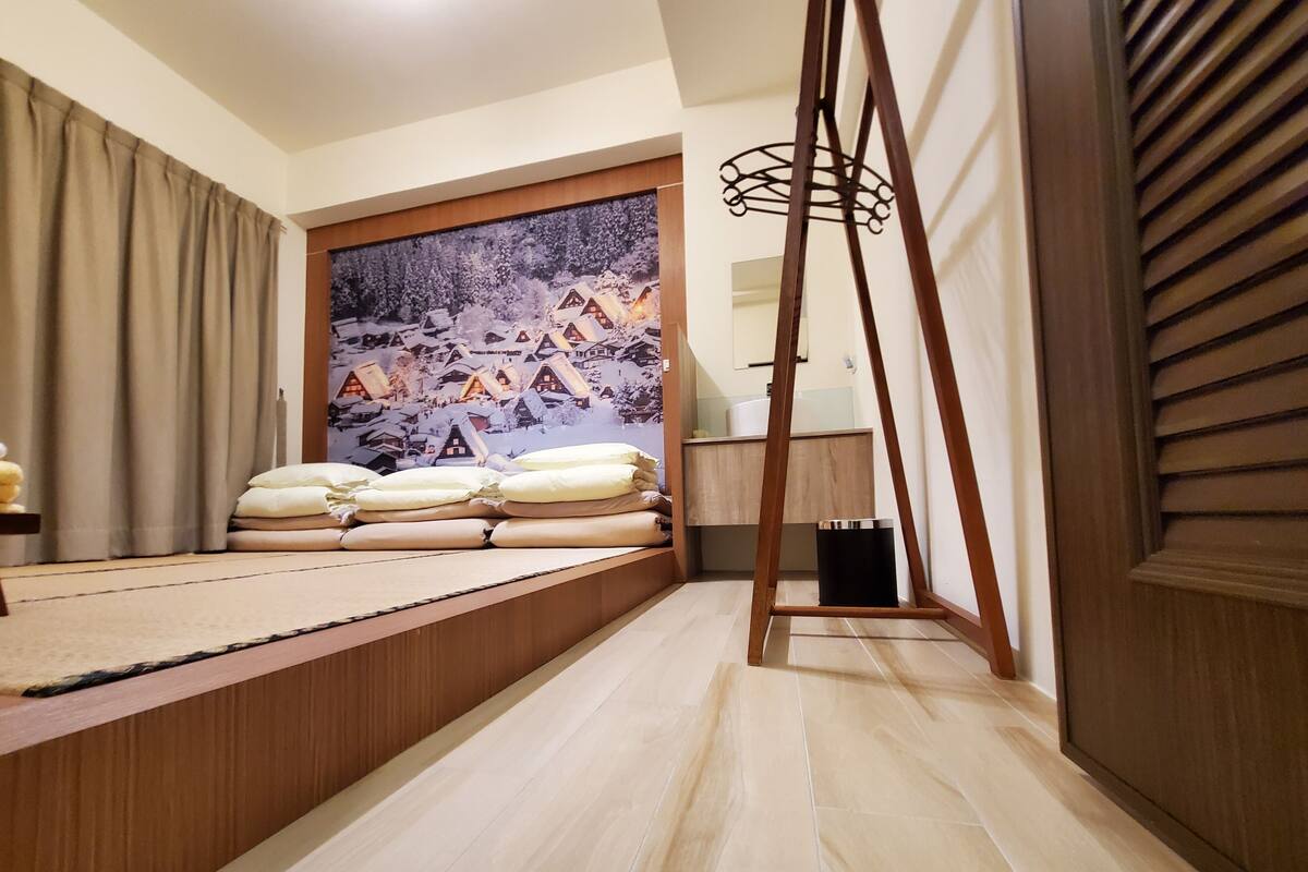 A bedroom with a bed, pillows, a wooden ladder, a trash bin, and a painting of a snowy village.
