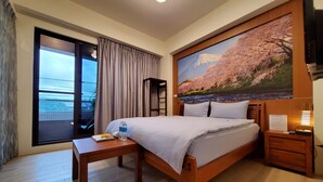 A hotel room with a bed, a bedside table, a nightstand, a large window with curtains, and a painting of cherry blossoms. - shanyue22 (Jiaoxi)
