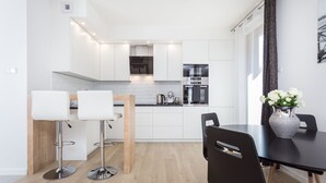 Eine moderne Küche mit weißen Schränken, Edelstahlgeräten und einem Essbereich mit einem schwarzen Tisch und Stühlen.