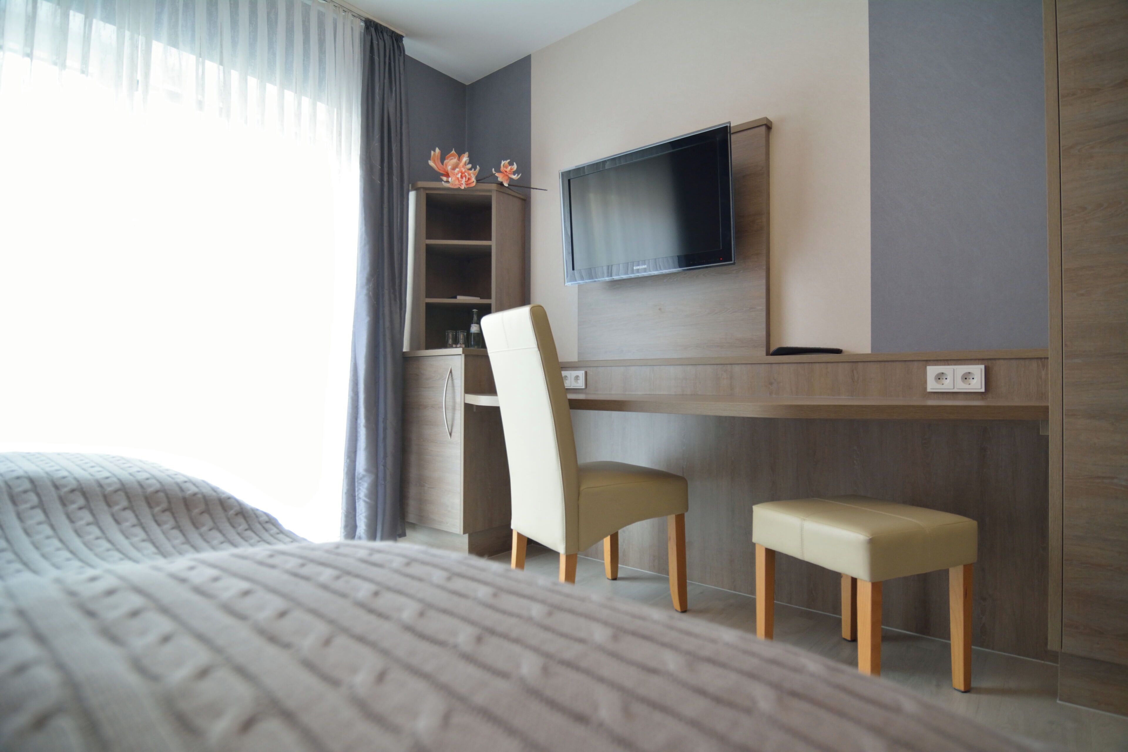 Una habitación de hotel con una cama, un escritorio con una silla, un televisor y un estante con objetos decorativos.