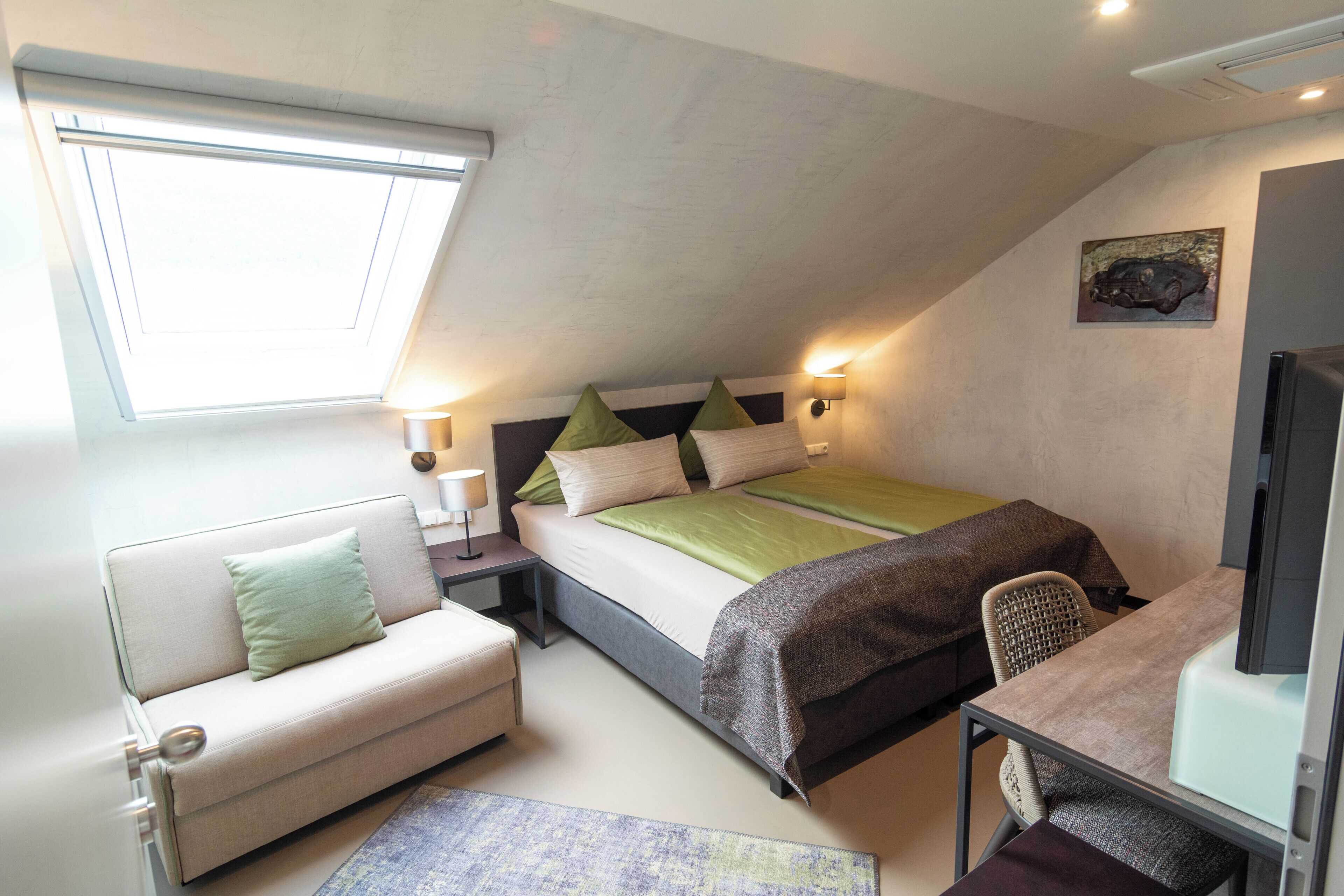 A bedroom with a bed, a desk, a chair, a sofa, a nightstand, and a window.