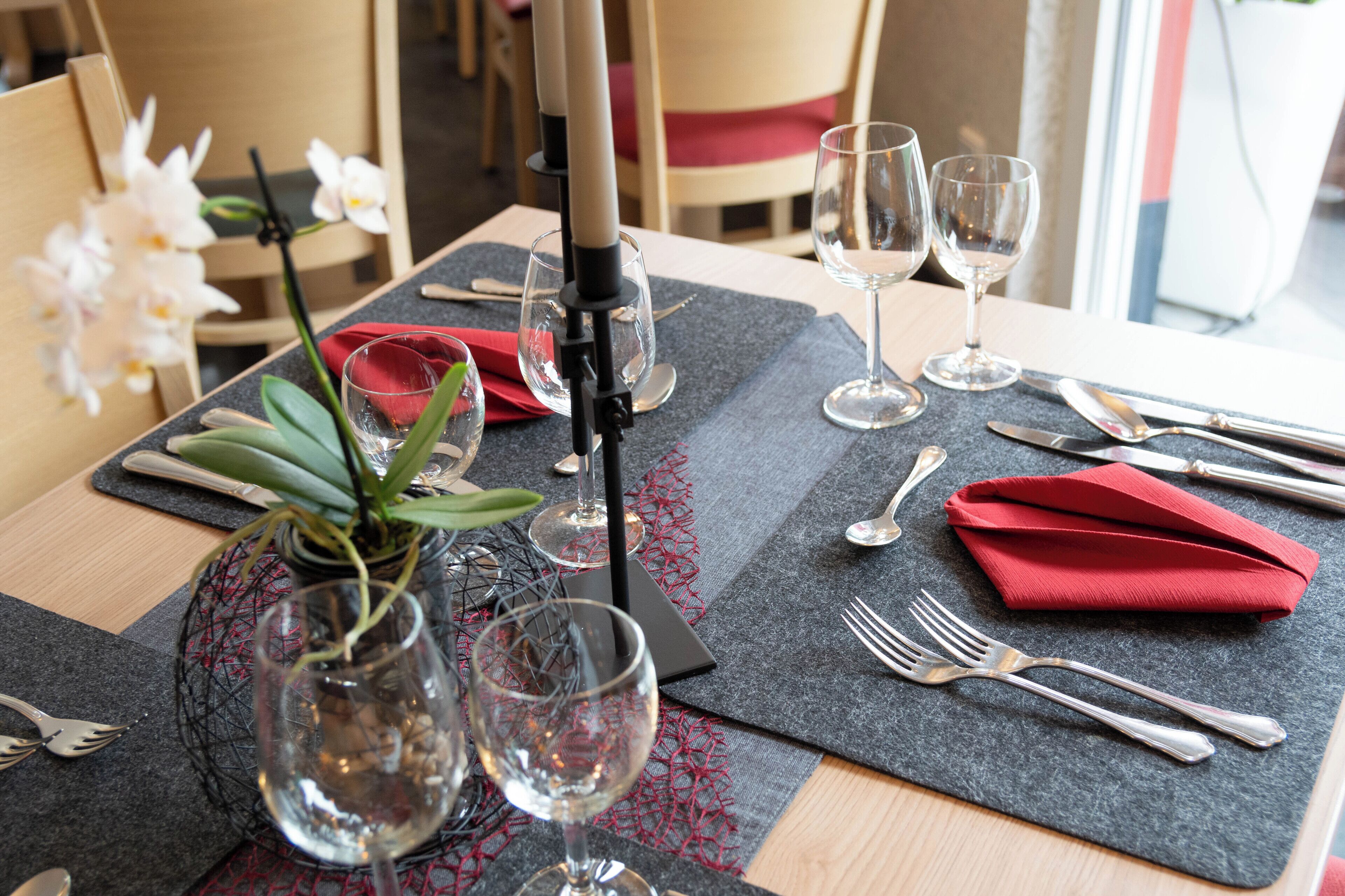 A dining table set with wine glasses, cutlery, and a red napkin.