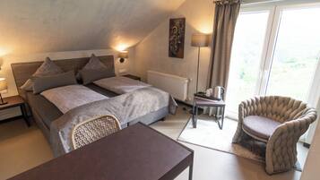 A bedroom with a double bed, bedside tables, a chair, a small table, and a view of the outdoors through a window.