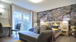 Een moderne slaapkamer met een grijze bank, een klein nachtkastje, een lamp en een stenen muur.