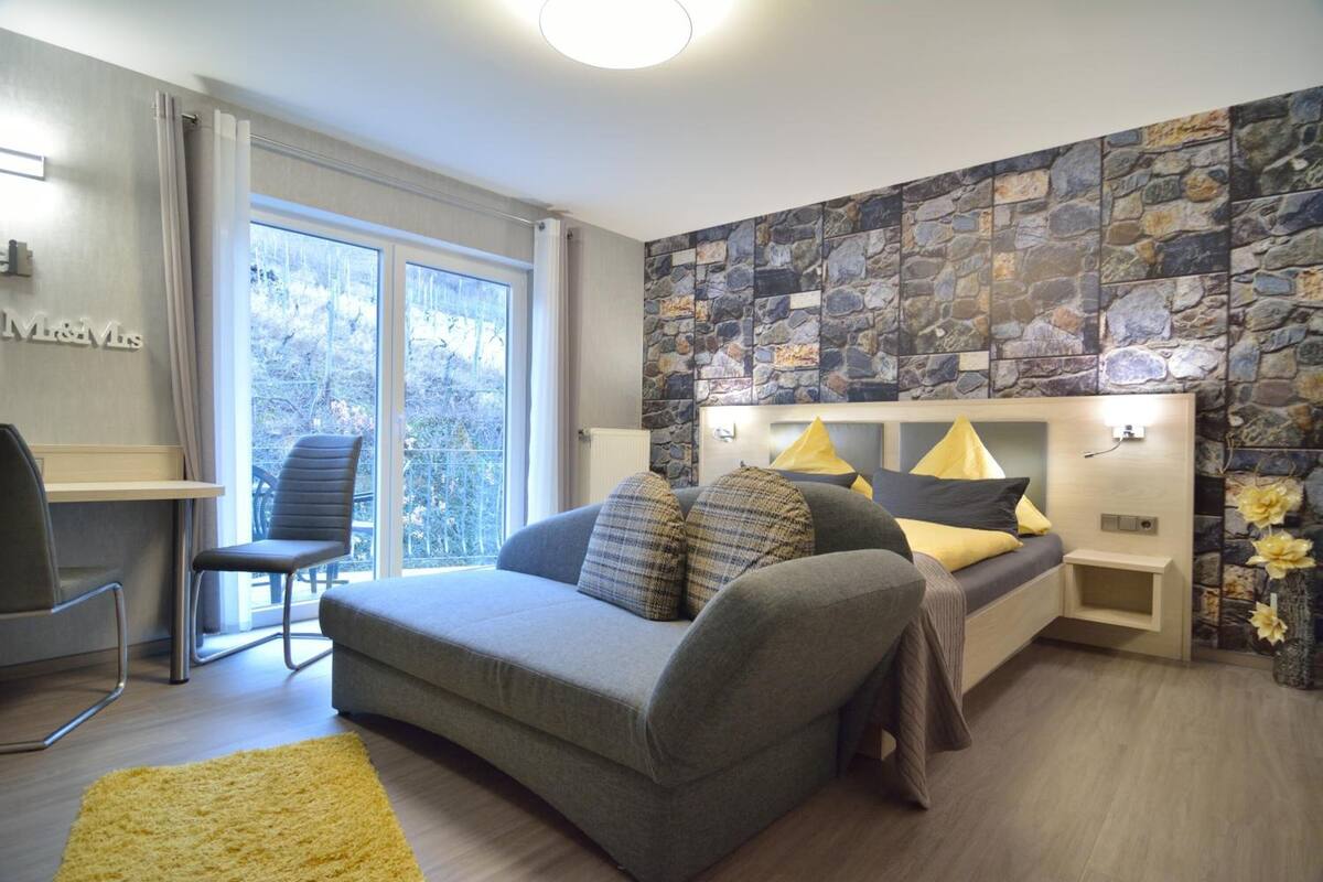 Een moderne slaapkamer met een grijze bank, een klein nachtkastje, een lamp en een stenen muur.