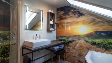 Ein modernes Badezimmer mit Dachfenster, einem großen Spiegel, einem weißen Waschbecken, einer Holz-Kommode und einer Badewanne.