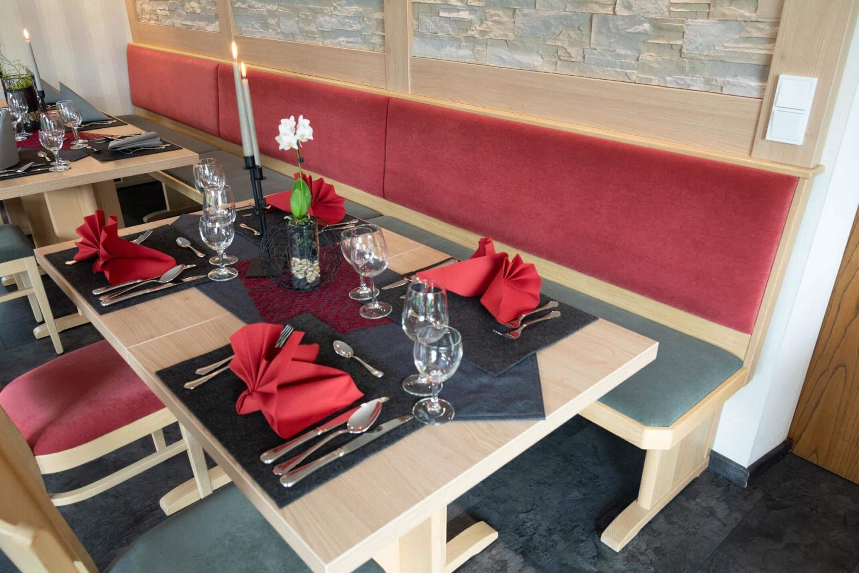 Un comedor con mesas de madera, bancos tapizados de rojo y posavasos negros.
