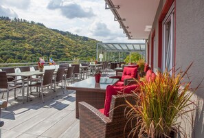 Un patio al aire libre con mobiliario de mimbre, una mesa de vidrio y cojines rojos.