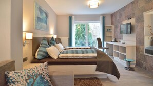 Een moderne slaapkamer met een bed, nachtlampjes, een televisie en een balkon met uitzicht op bomen.