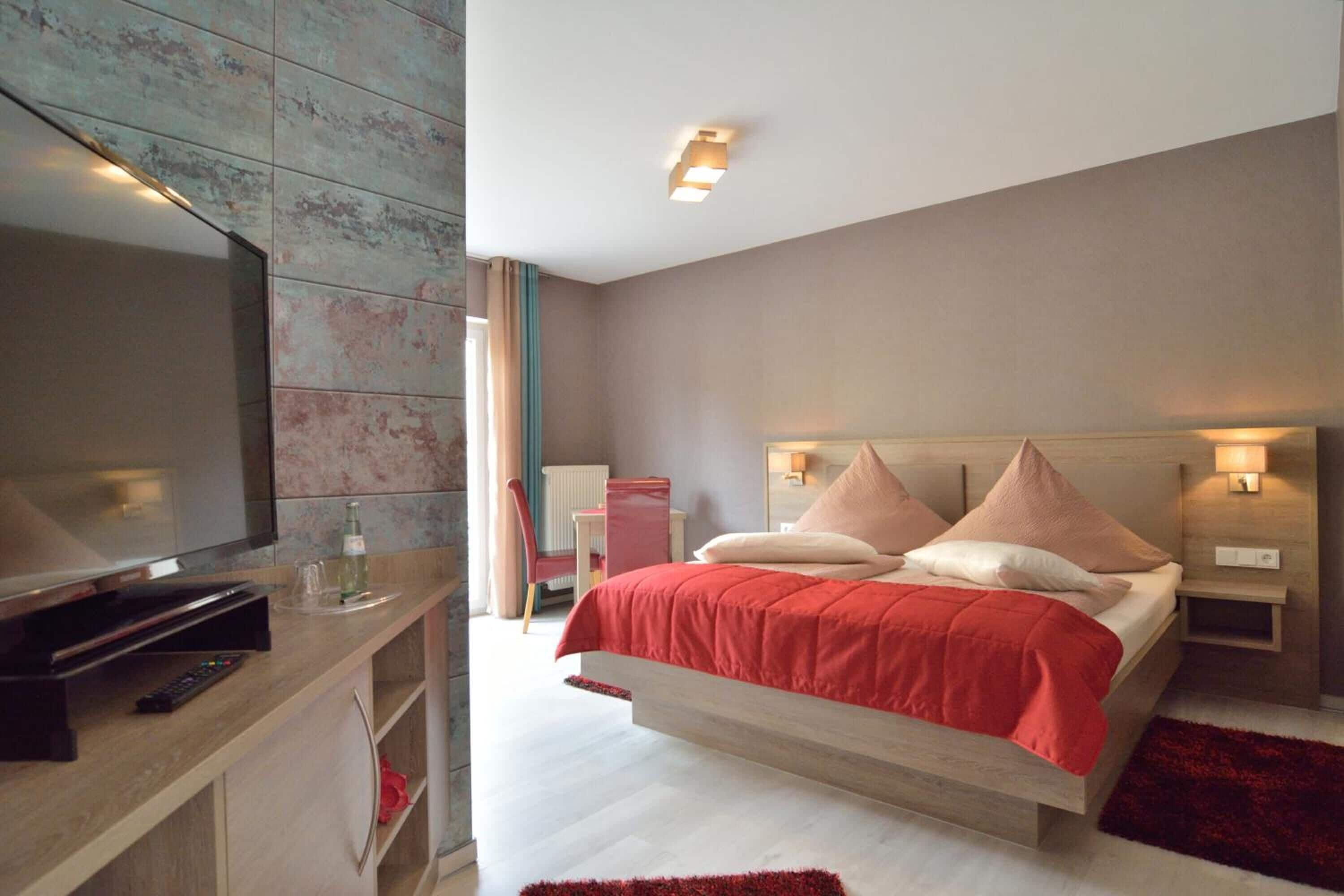 A modern bedroom with a large bed, bedside tables, a TV, and a red rug.