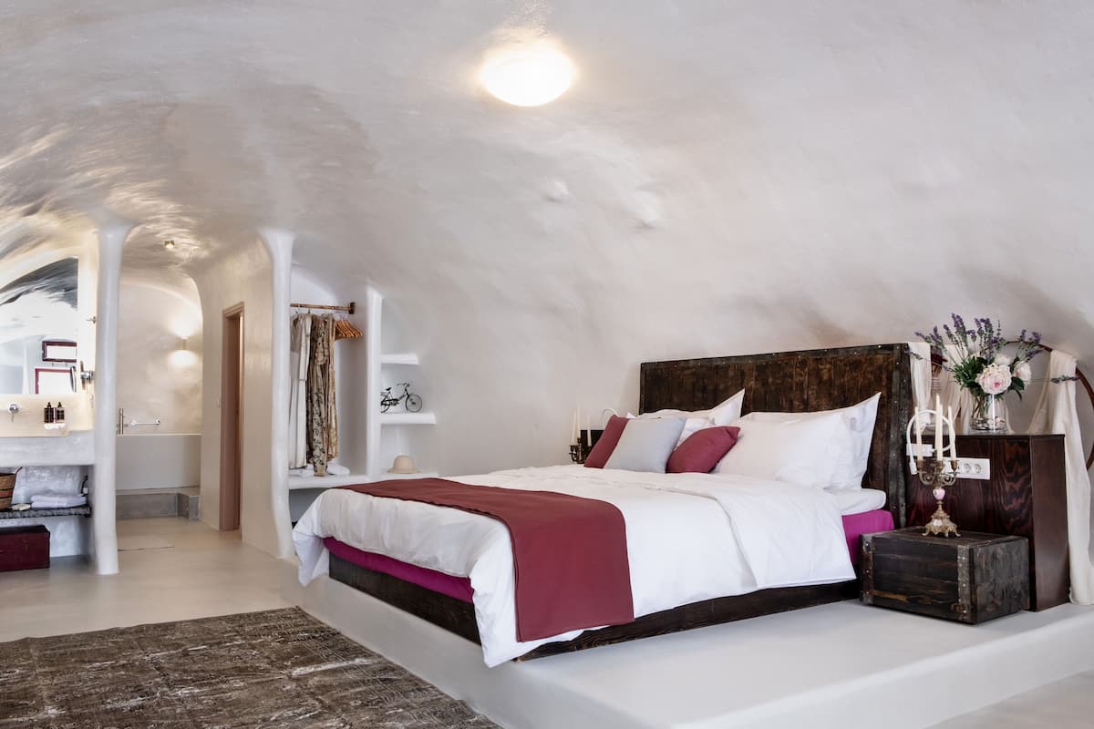 Een slaapkamer met een groot bed, een kaptafel met spiegel en een klein tafeltje met een kaars.