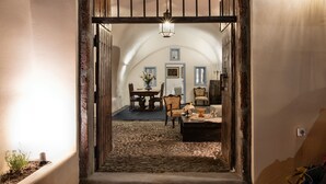 Un couloir rustique mène à une salle à manger où se trouvent une table et des chaises, un lustre et une porte à cadre en bois.