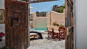 Une porte en bois rustique donne sur un espace extérieur ensoleillé, aménagé avec une piscine, une table et des chaises.