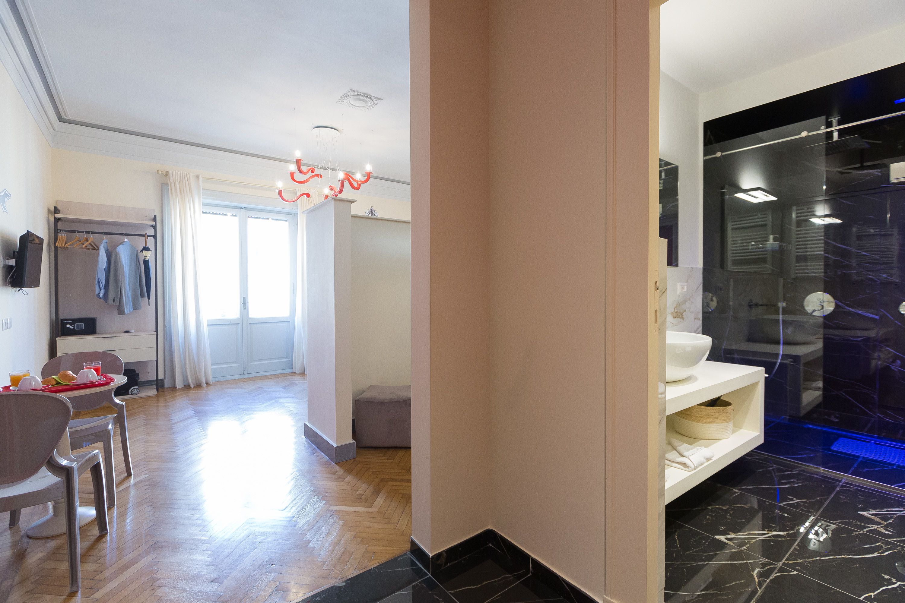 A modern hotel room with a wooden floor, a bathroom with a glass shower, and a dining area with a table and chairs.