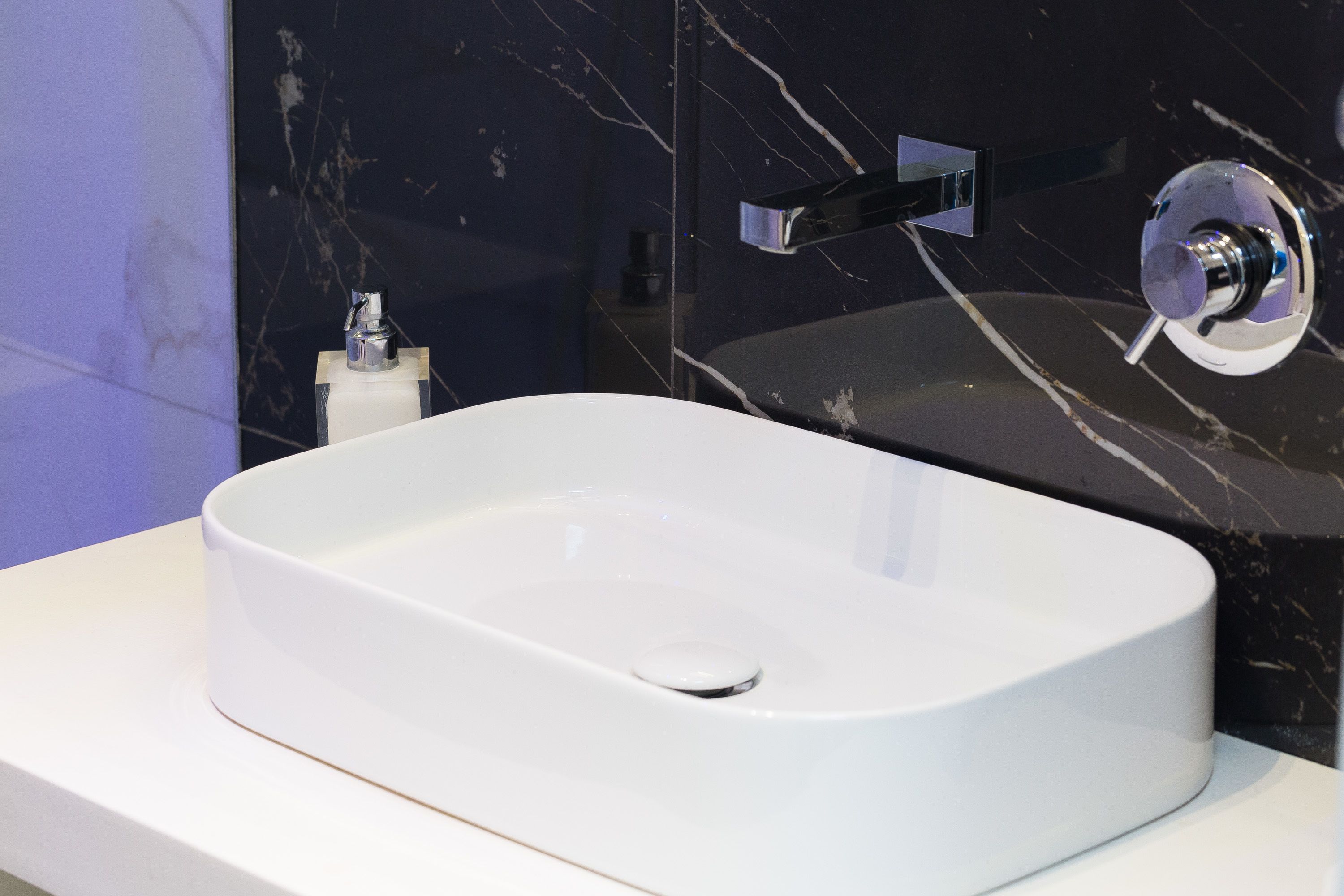Une salle de bain moderne avec un lavabo blanc, des murs en marbre noir et un robinet chromé.