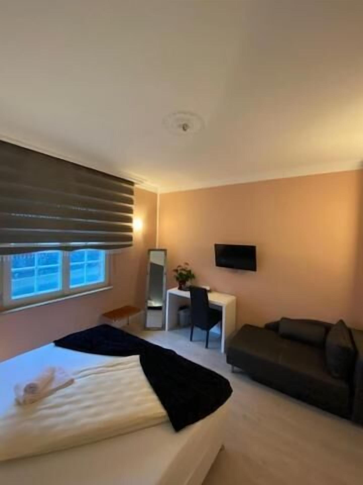 A bedroom with a bed, a desk, a chair, a sofa, and a TV mounted on the wall.