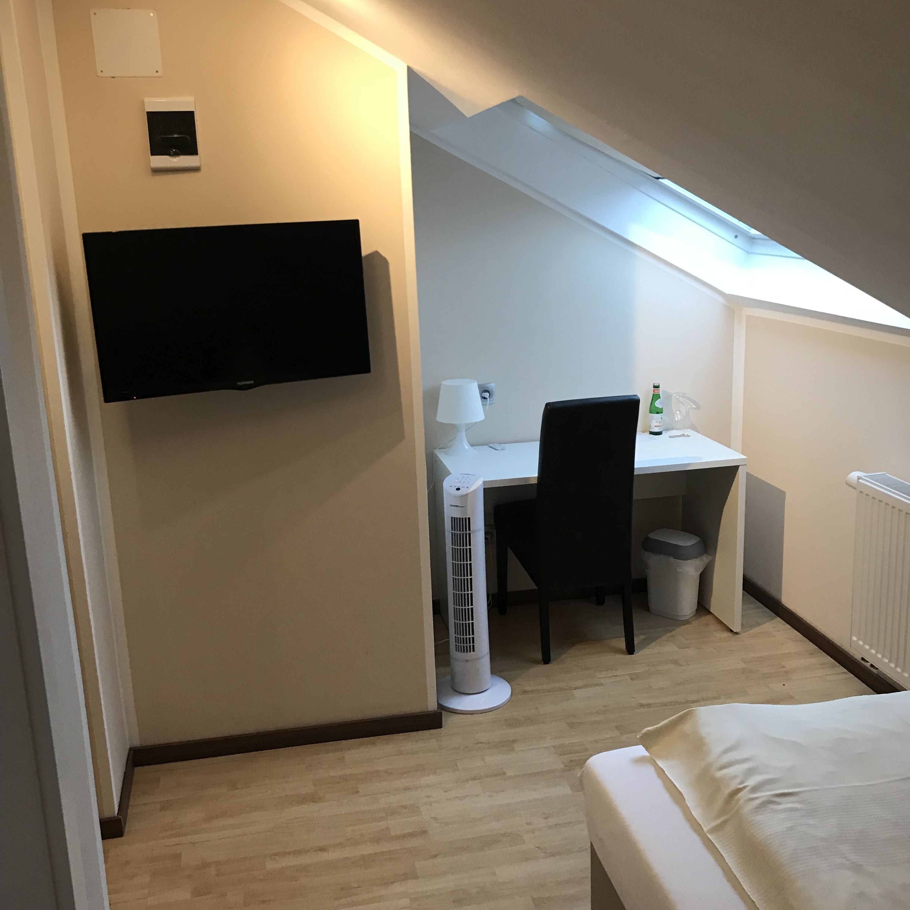 A compact room with a bed, a desk, a chair, a TV, a lamp, and a radiator.
