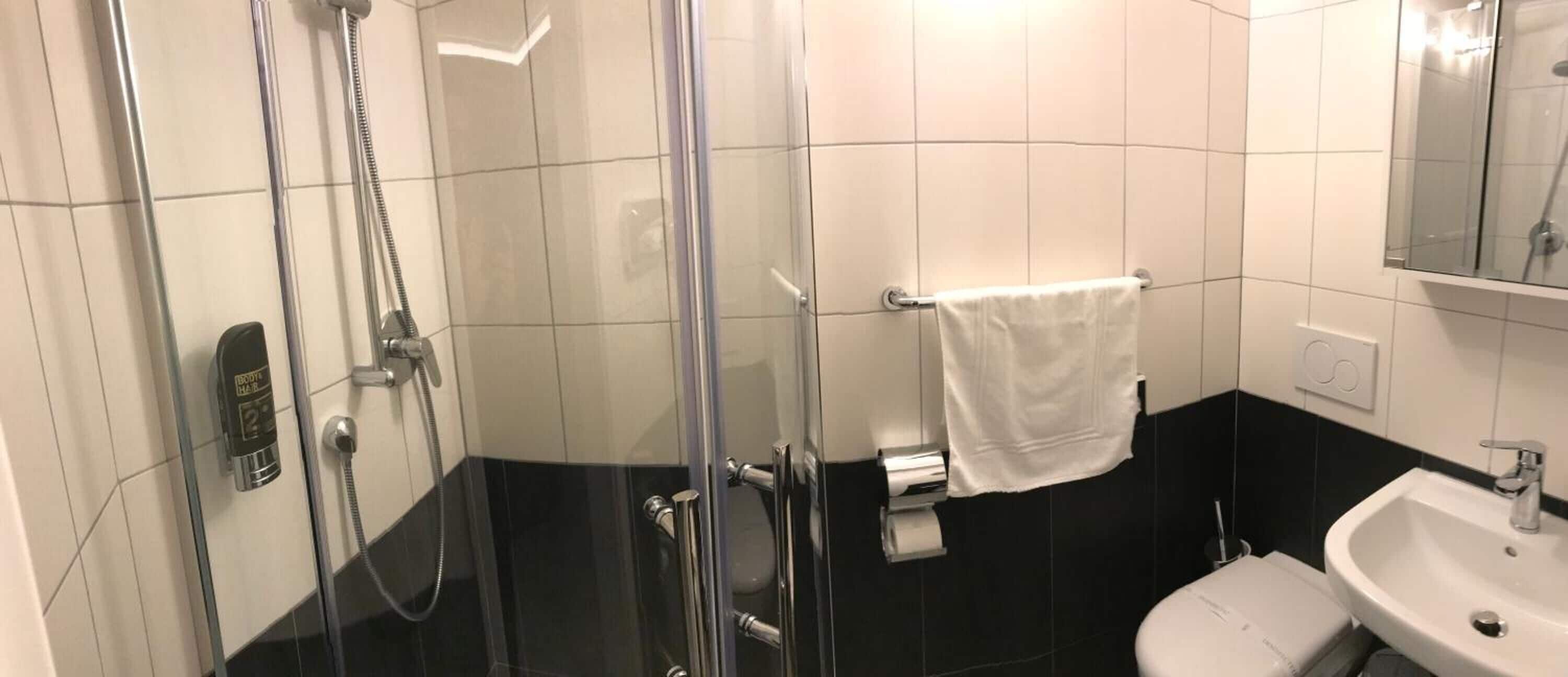 Un baño con ducha de vidrio, un lavamanos blanco y un perchero para toallas.