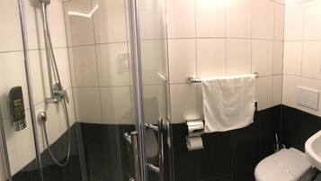Un baño con ducha de vidrio, un lavamanos blanco y un perchero para toallas.