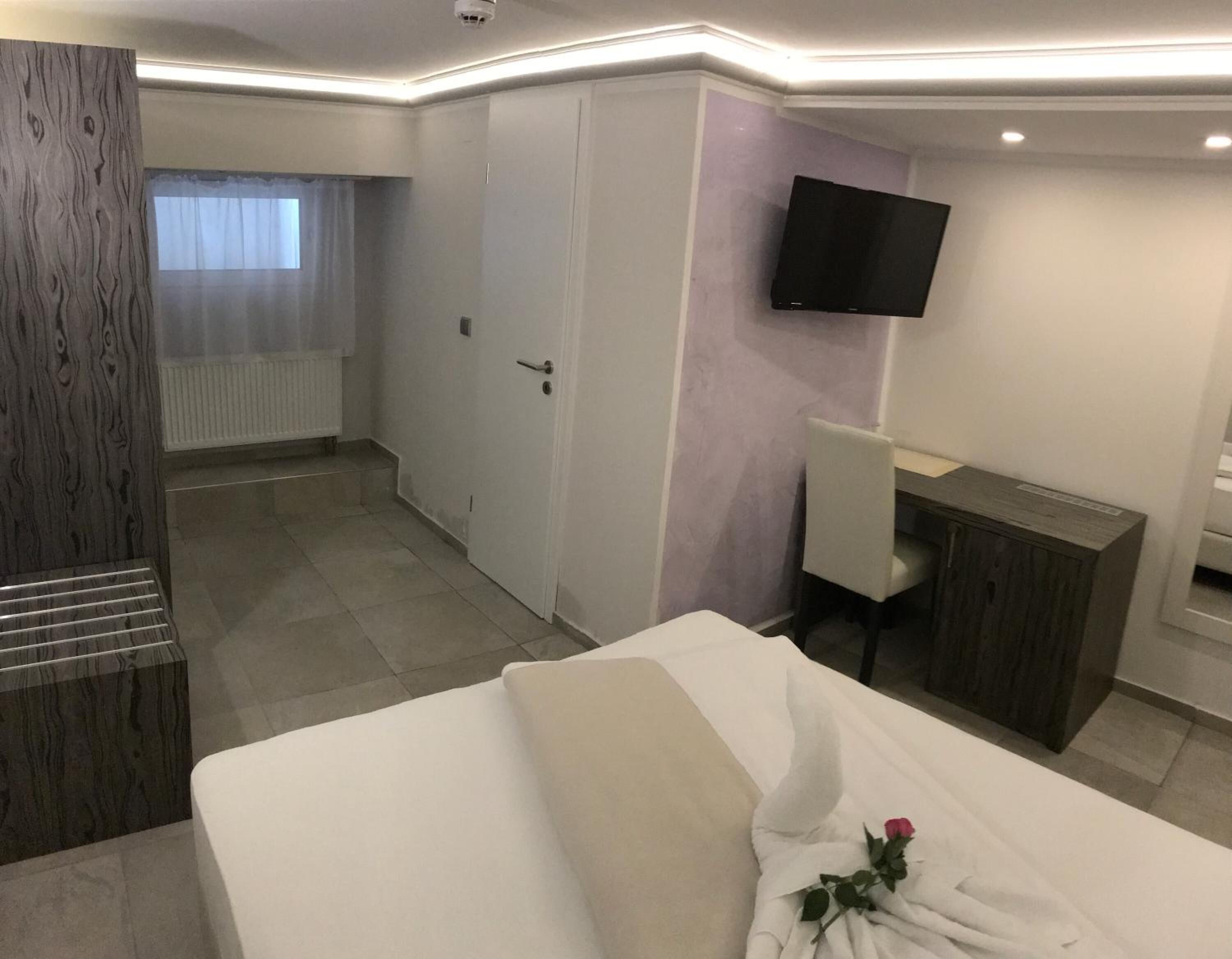 A hotel room with a bed, a desk, a chair, a TV mounted on the wall, and a window with curtains.