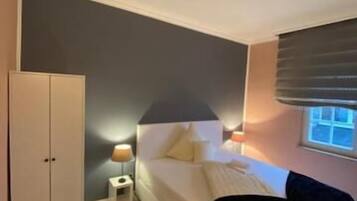 A bedroom with a bed, bedside table, lamp, wardrobe, and a window.