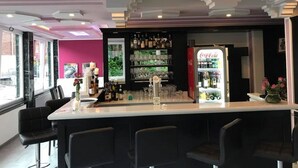 Een bar met een toonbank, barstoelen, planken vol flessen en glazen, en een Coca-Cola koelkast.