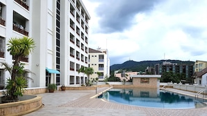 A swimming pool area with a tiled deck, surrounded by buildings with balconies and a mountain in the background. - Napas Residence (Hat Yai)