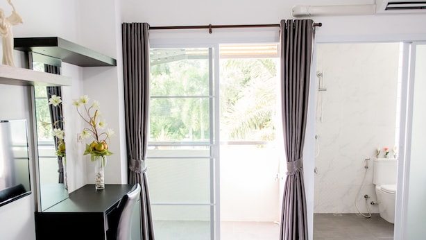 A modern hotel room with a bed, a desk with a chair, a vanity with a mirror, and a bathroom with a toilet and sink. - Napas Residence (Hat Yai)
