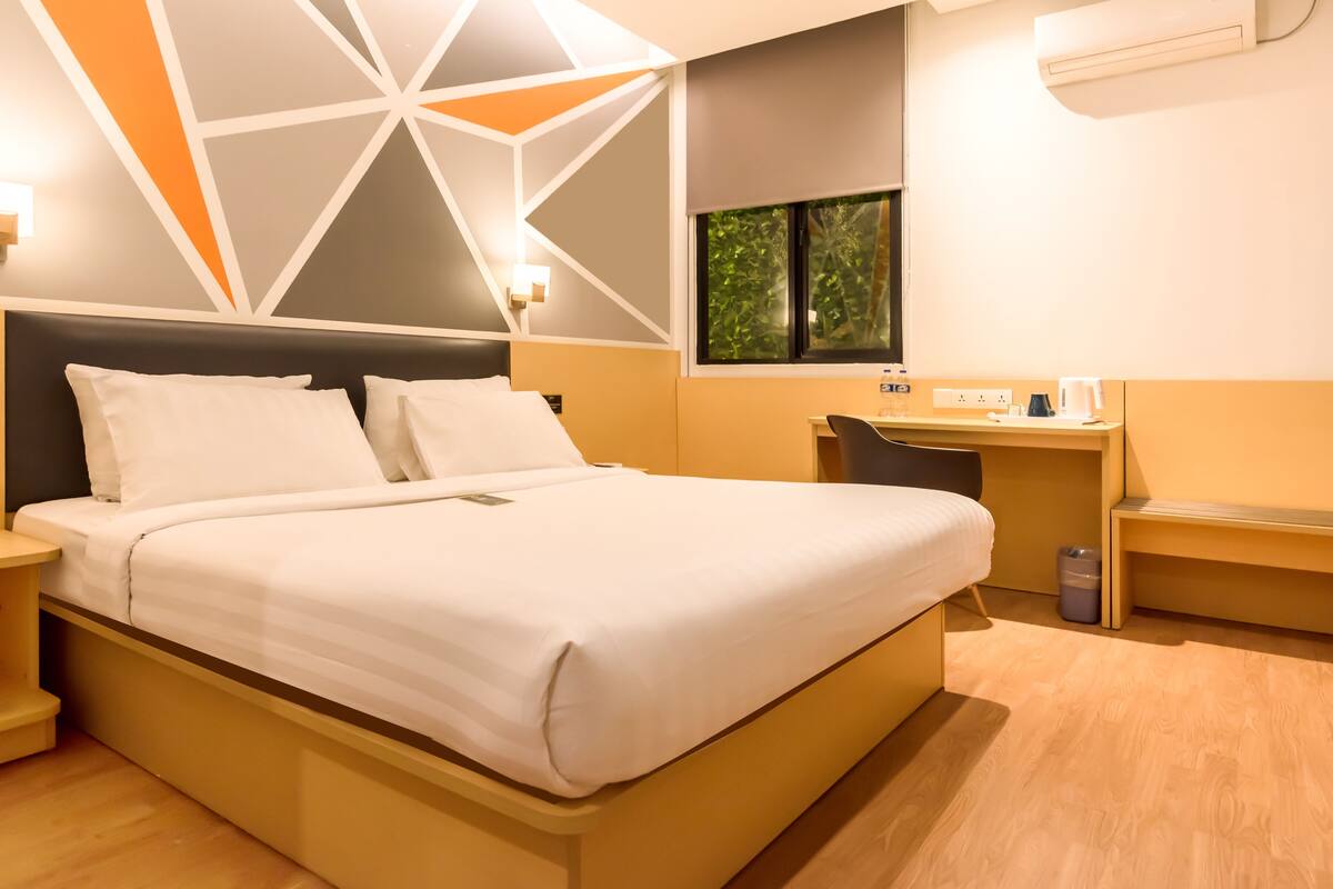 Een moderne hotelkamer met een bed, nachtkastjes, een bureau en een raam met uitzicht op groen.