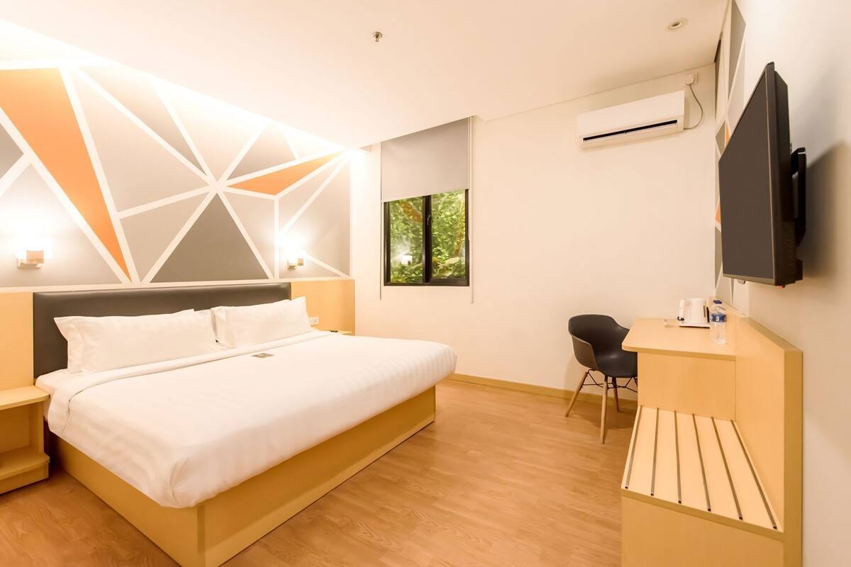 Een moderne hotelkamer met een bed, nachtkastjes, een bureau, een stoel, een televisie en een airconditioning.